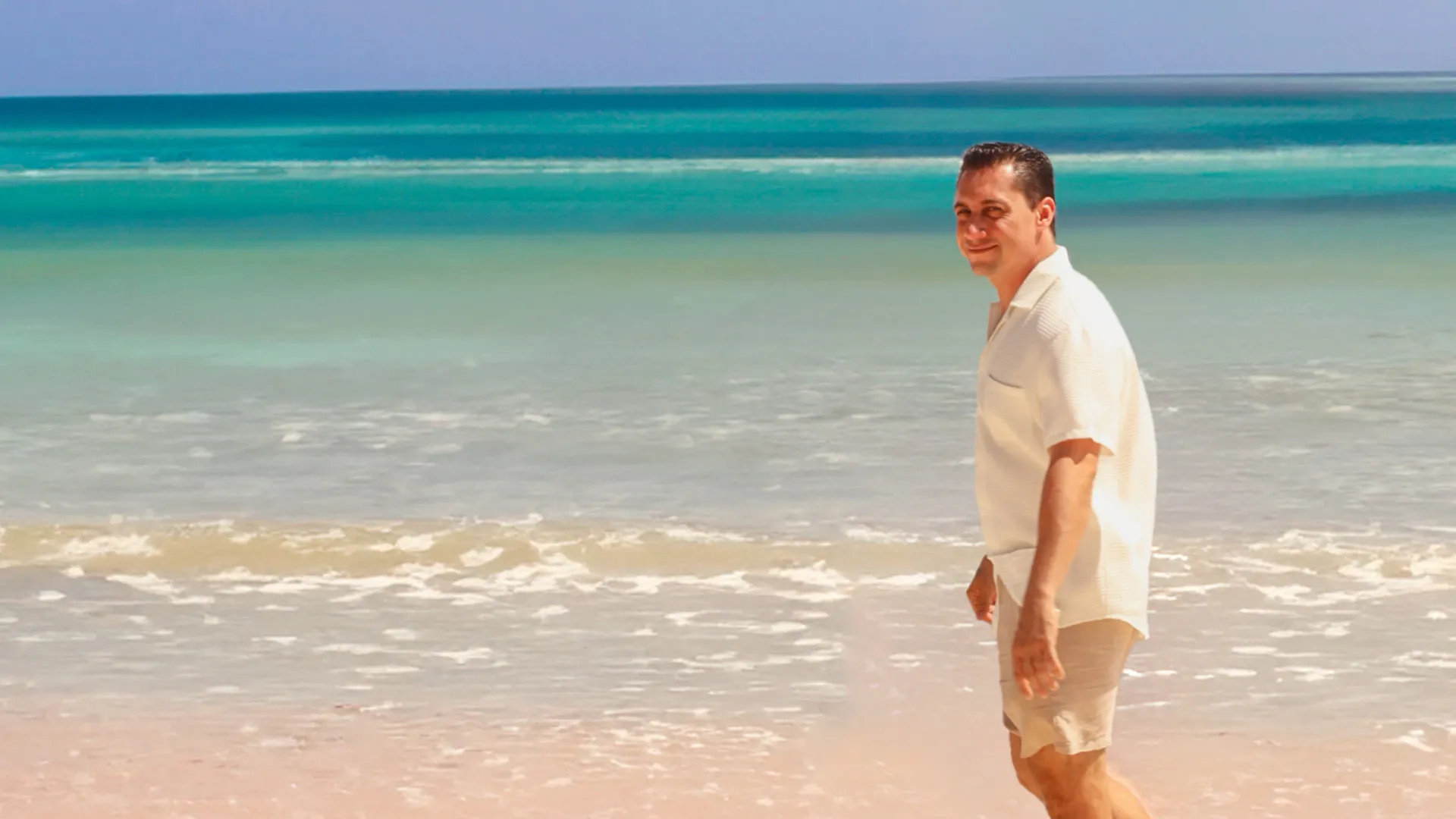 Sergio Tavares caminando por una playa de arena blanca frente al mar Caribe turquesa en la Riviera Maya